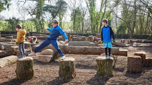 Three young boys hop along wood rounds in Dyffryn Gardens' play area